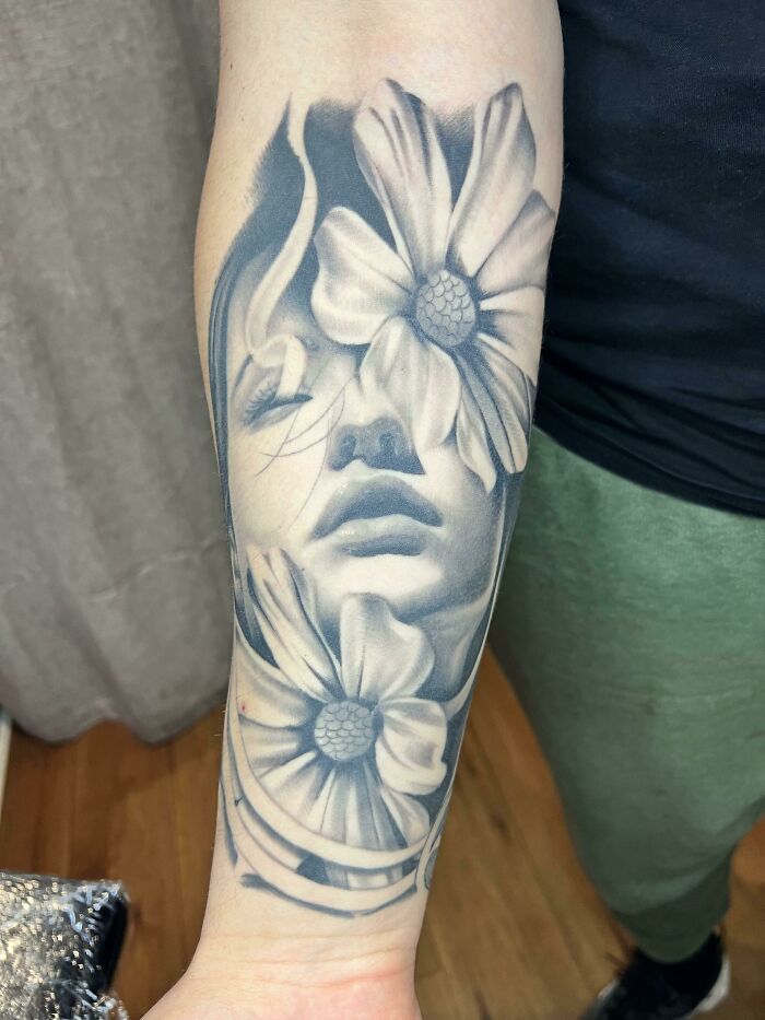 Floral tattoo with a woman's face and blossom design on the forearm.