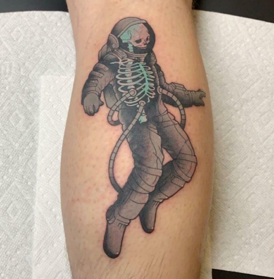 Tattoo of an astronaut with a skeleton design, showcasing outer space cool style on a person's leg.