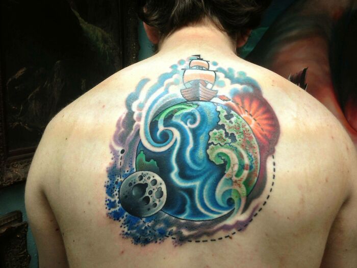 Colorful space tattoo on a person's back featuring the Earth, moon, waves, sun, and ship.