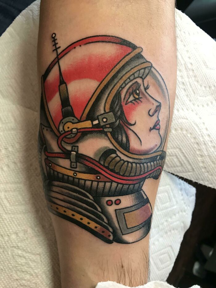 Astrology-themed space tattoo featuring a colorful astronaut helmet on a forearm.