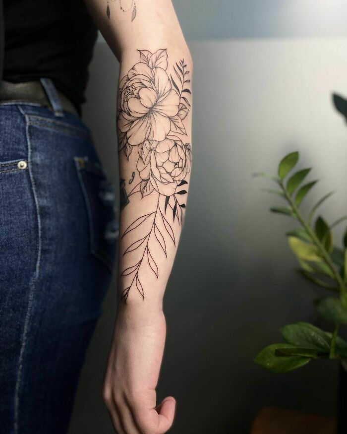 Floral tattoo design on a forearm with detailed leaves, showcasing realistic flower tattoos.