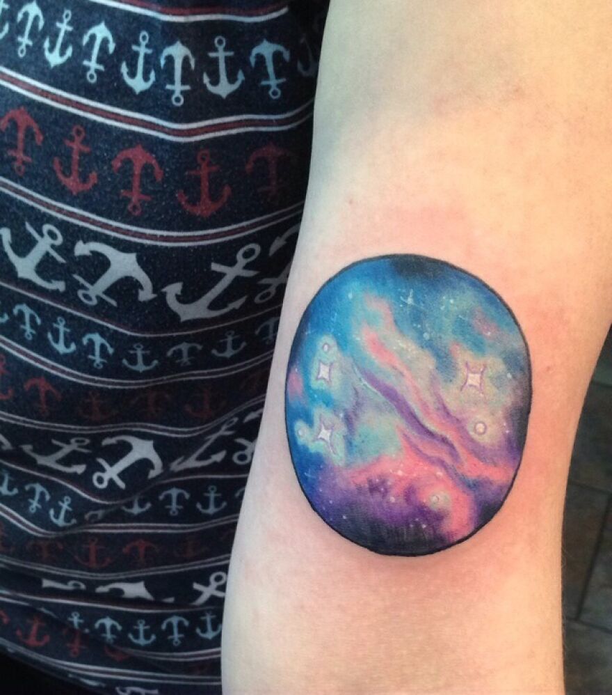 Space tattoo featuring a colorful galaxy design on a person's arm, with a patterned anchor shirt in the background.