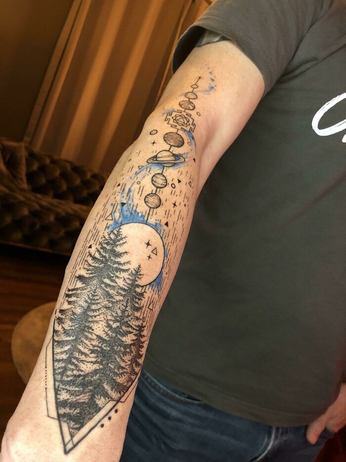 Astrology-themed space tattoo with planets and trees on a person's forearm.