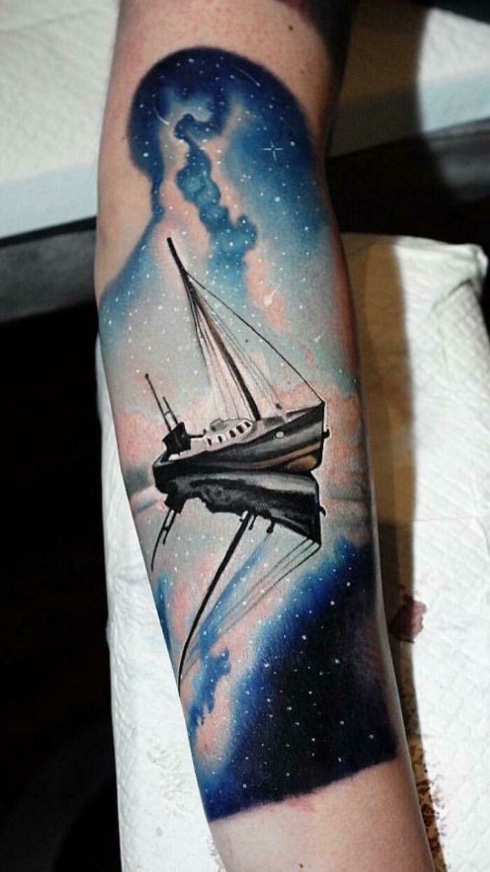 Space tattoo featuring a sailboat against a cosmic night sky with stars and nebula on an arm.