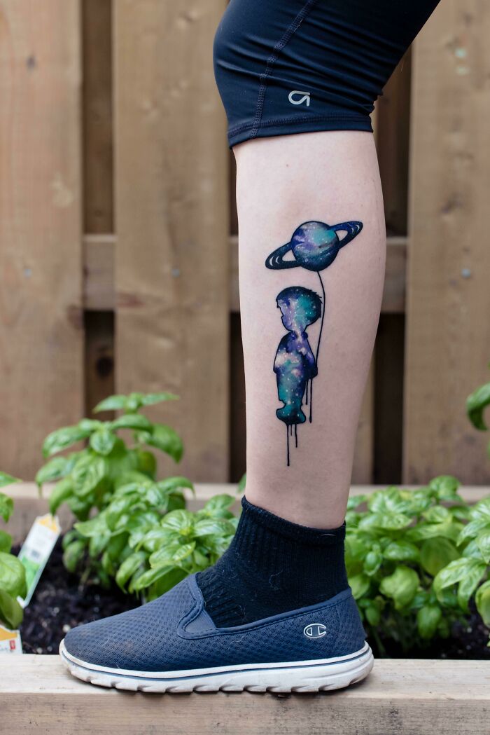 Space tattoo of a galaxy-themed silhouette holding a planet balloon on a person's calf.