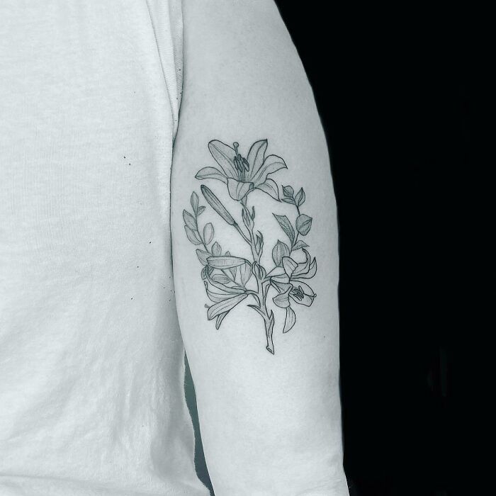 Flower tattoo on arm, featuring detailed blossoming lilies and leaves in black ink.