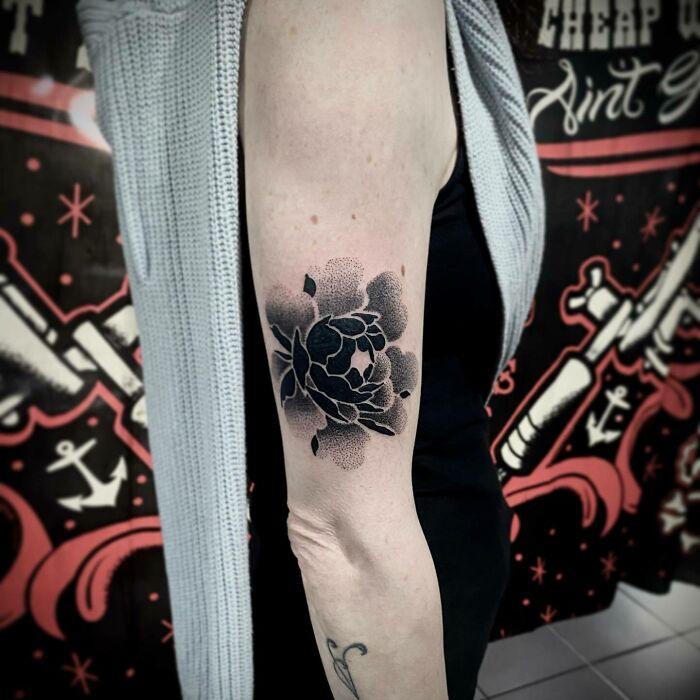 Arm adorned with an elegant black flower tattoo against a colorful background.