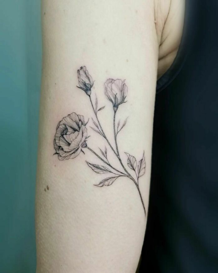 Delicate flower tattoo with buds and leaves on forearm, showcasing intricate floral designs.