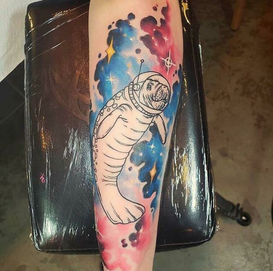 Space tattoo of an astronaut seal with colorful galaxy background on forearm.