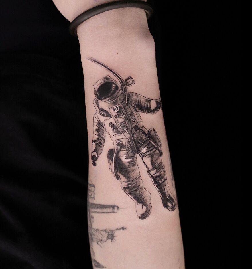 Astronaut tattoo on forearm, detailed black ink design for space and astrology enthusiasts.