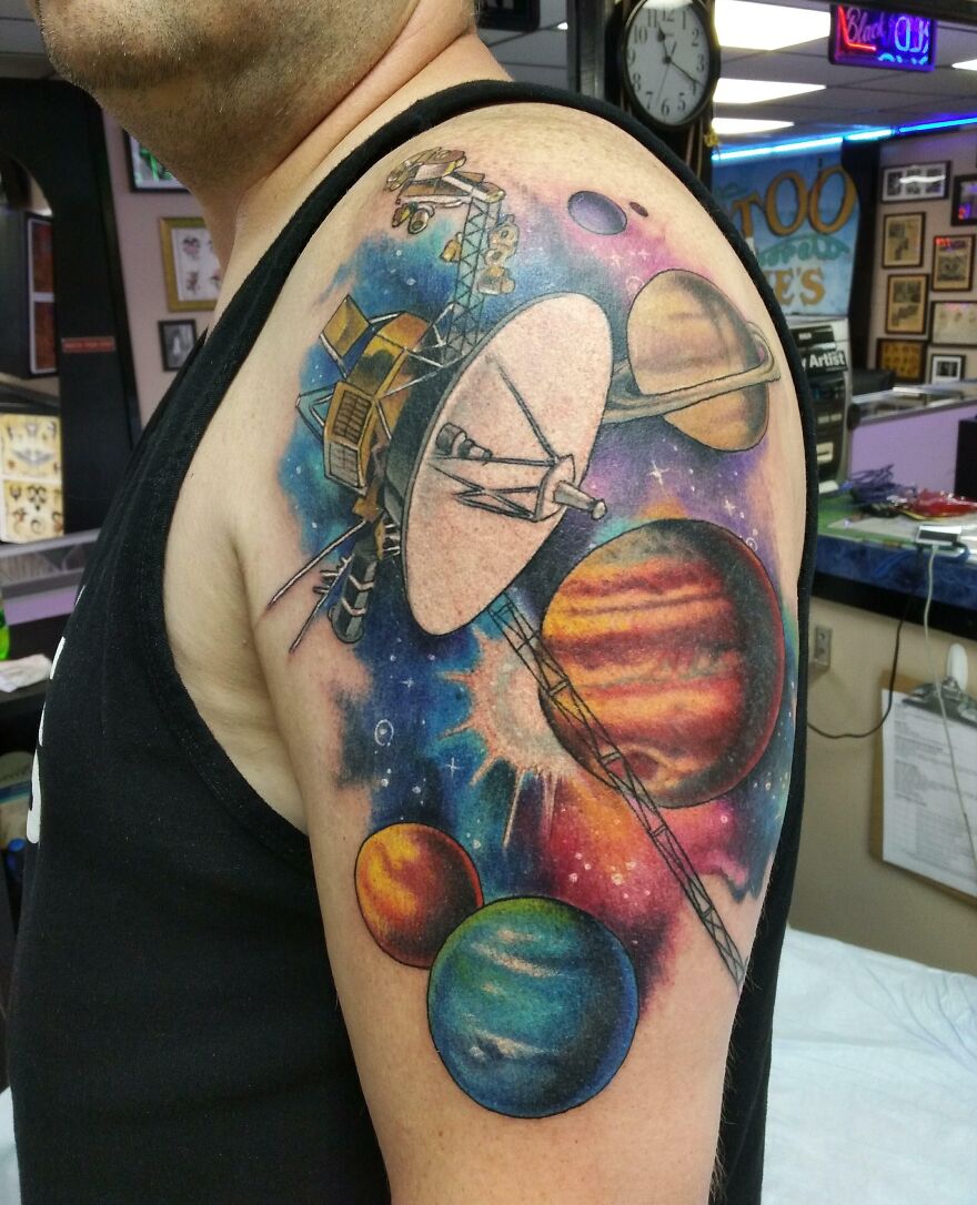 Space tattoo featuring planets and a satellite on an arm, showcasing vibrant outer space colors.