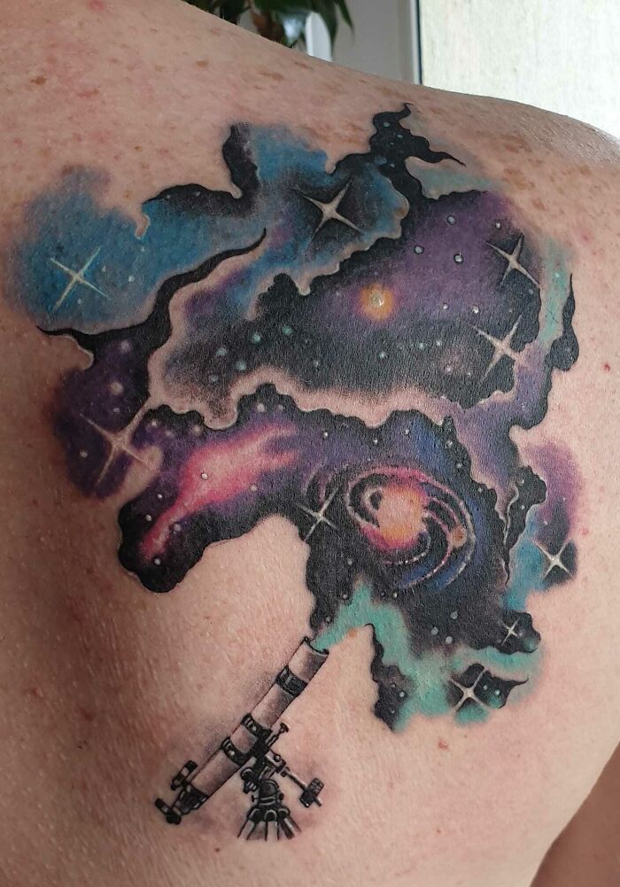 Cosmic space tattoo with a galaxy and telescope design on a person's shoulder.