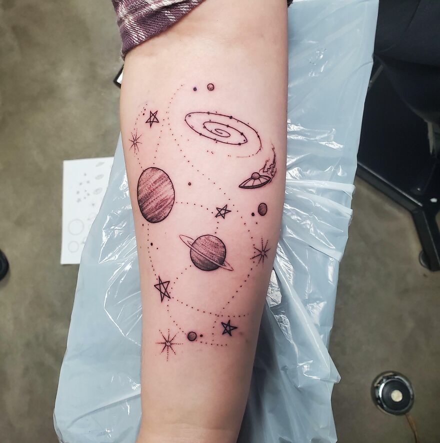 Space tattoo featuring planets, stars, and a galaxy design on a forearm.