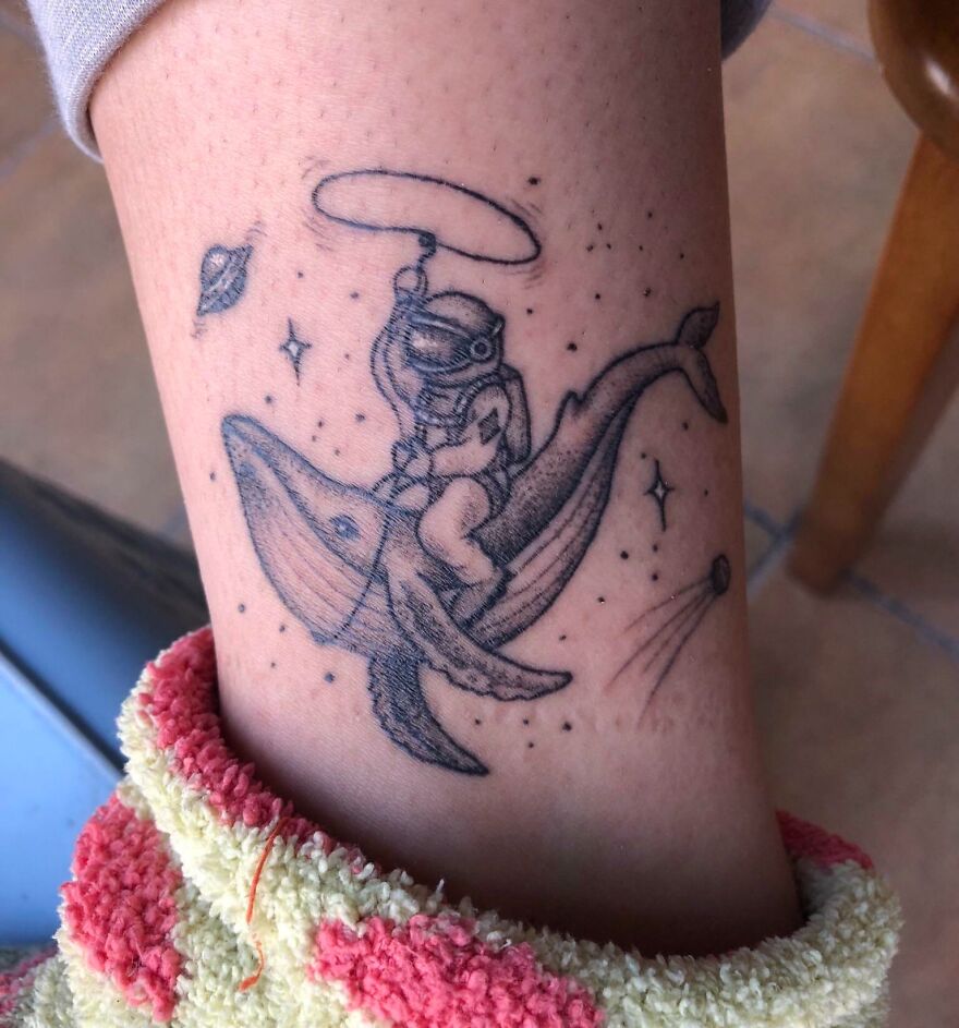 Astronaut riding a whale tattoo with planets and stars; a space tattoo for astrology fans.