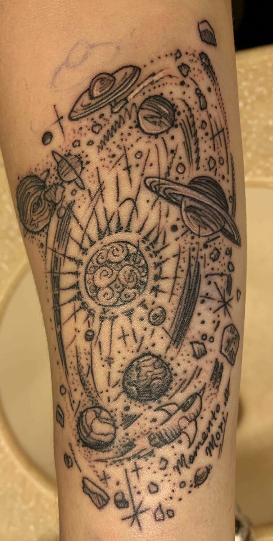 Outer space tattoo featuring planets, stars, and cosmic elements on forearm.