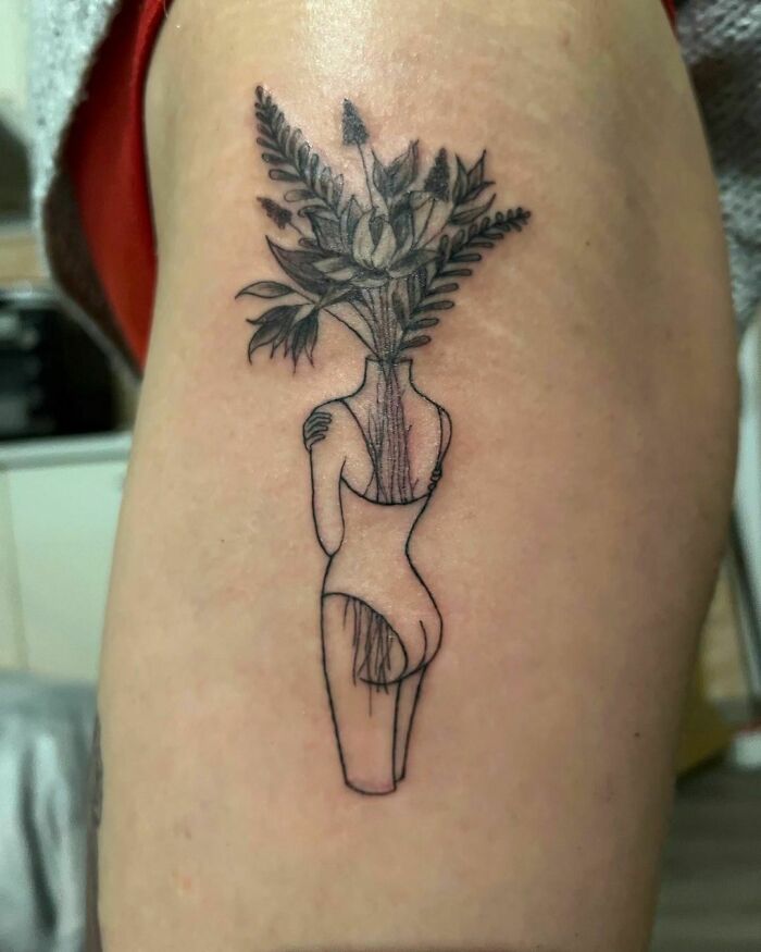 Self-love tattoo of a person hugging themselves with flowers as a head, symbolizing growth and self-acceptance.