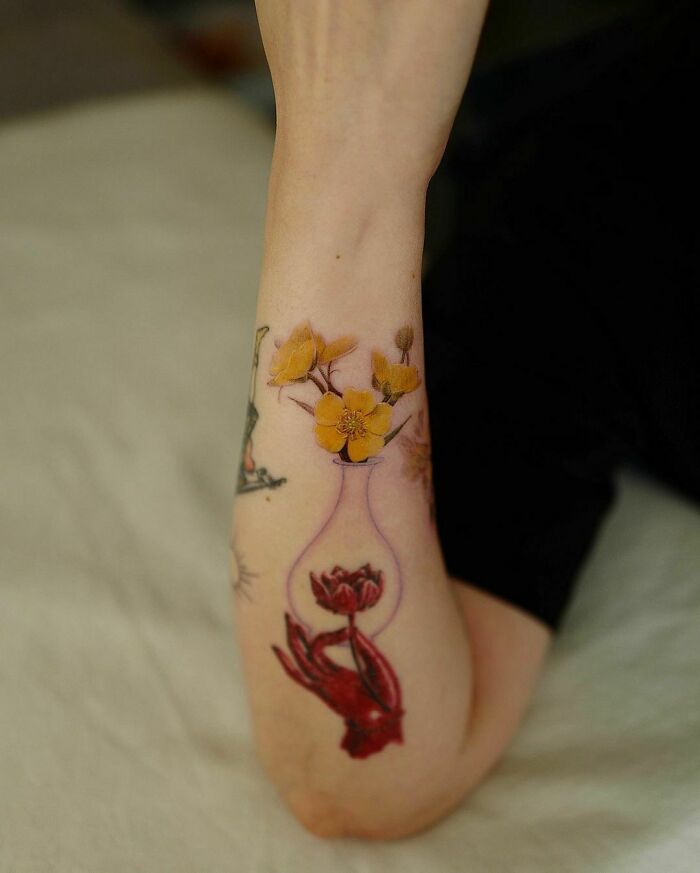 Flower tattoo on forearm with vibrant yellow blossoms and a vase design.