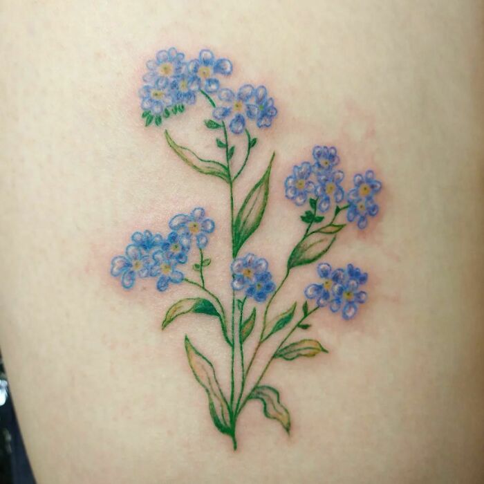 Floral self-love tattoo featuring blue forget-me-not flowers on skin.