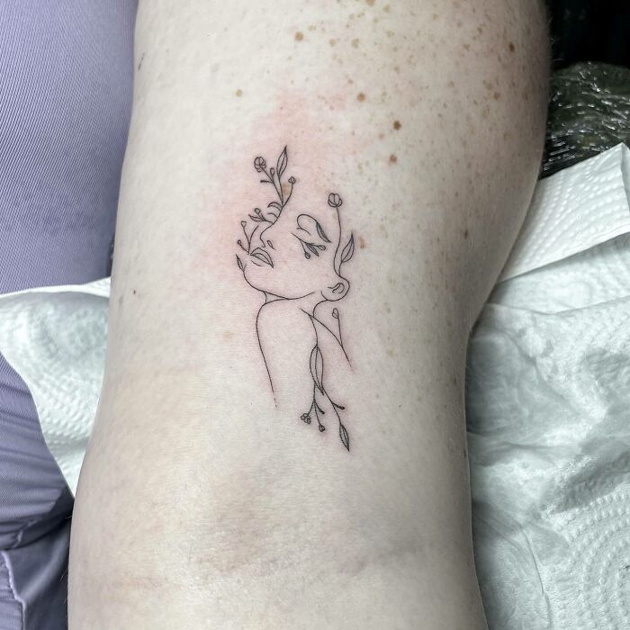 Line art flower tattoo on skin, showing a face intertwining with floral elements.