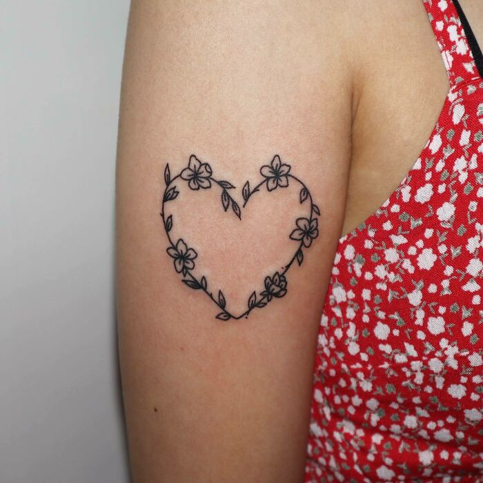 Floral heart tattoo on arm, flowers and leaves outlining the shape in delicate black ink.