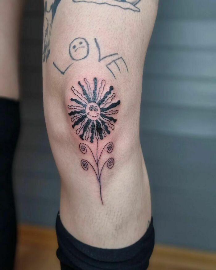 Flower tattoo on knee, featuring a smiling sun with swirling petals, alongside the word "love" tattooed above.