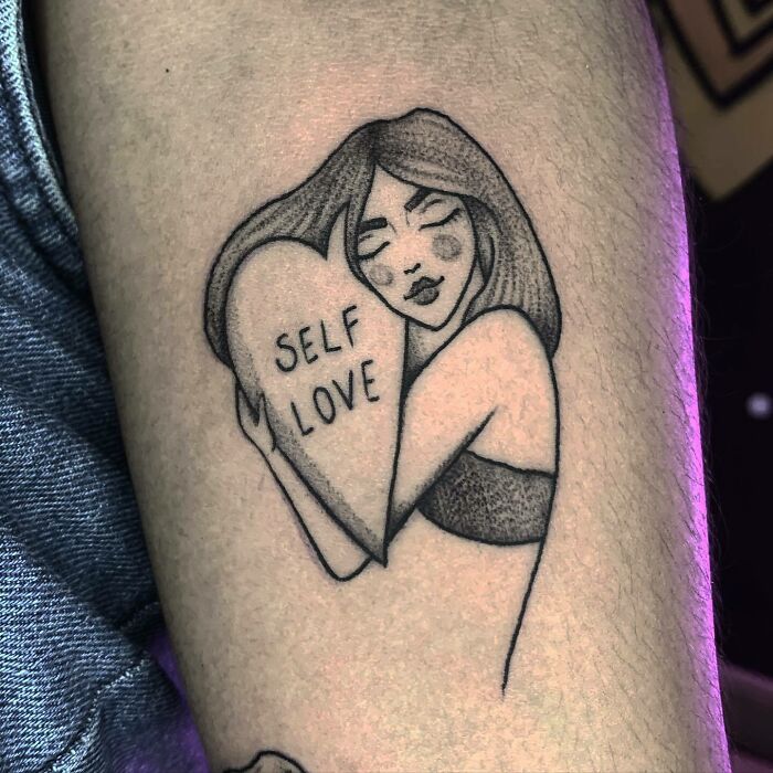 Tattoo of a woman hugging a heart with "Self Love" inscription, highlighting self-love.