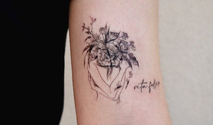 Self-love tattoo of flowers and hands with the phrase "vita felix" on an arm, symbolizing personal growth and empowerment.