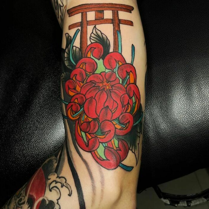 Red flower tattoo on forearm, vibrant petals intertwining with Japanese torii gate design.