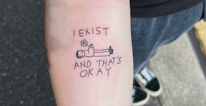 Self-love tattoo with person holding a flower, featuring the text "I exist and that's okay," promoting self-acceptance.