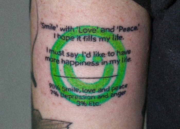 Self-love tattoo with a green smiley face and positive text promoting happiness and peace on the upper arm.