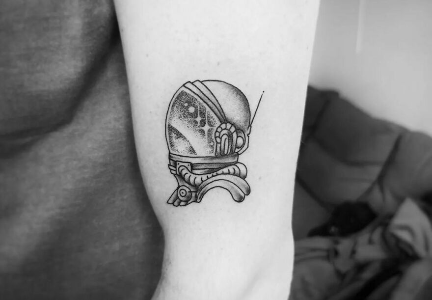 Astronaut helmet space tattoo on arm, showcasing intricate black ink design.