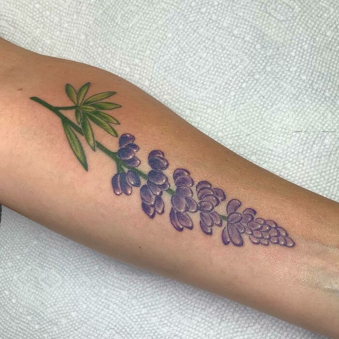 Purple flower tattoo on forearm, illustrating delicate floral design blossoming on the skin.