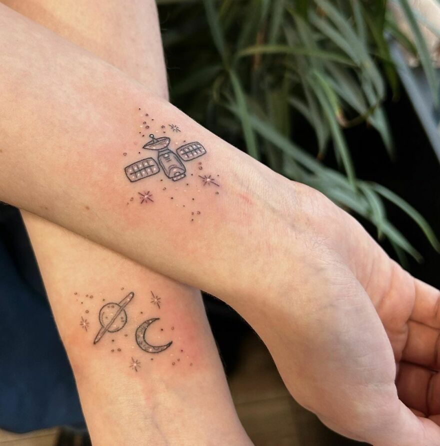 Space tattoos featuring a satellite, planet, and crescent moon on forearms with star details.
