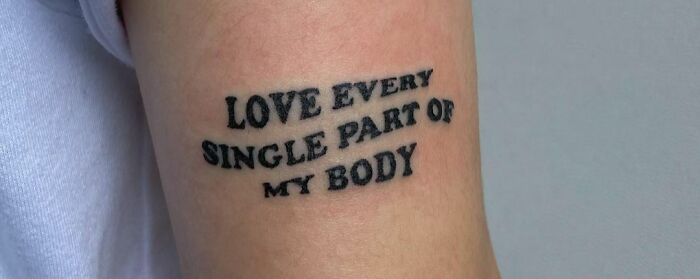 Self-love tattoo reading "Love every single part of my body" on an arm.