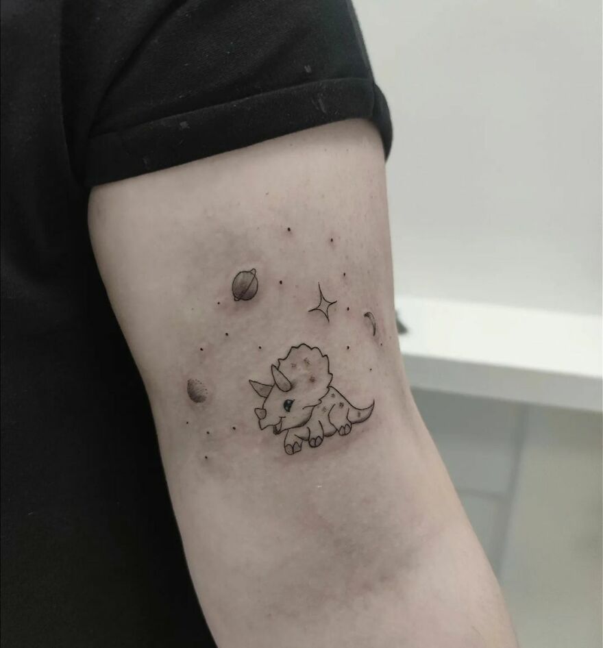 Arm with a space tattoo featuring a cute triceratops and planets, appealing to astrology fans.
