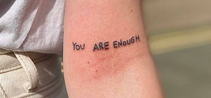 Self-love tattoo featuring "You Are Enough" on an arm.