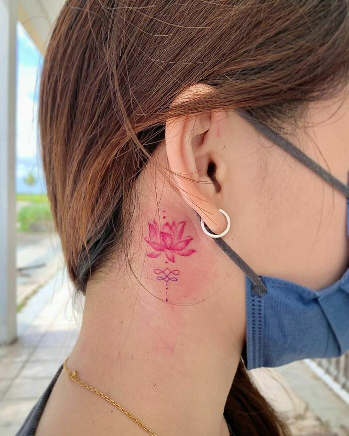 Delicate pink lotus flower tattoo behind ear, showcasing elegance and beauty.