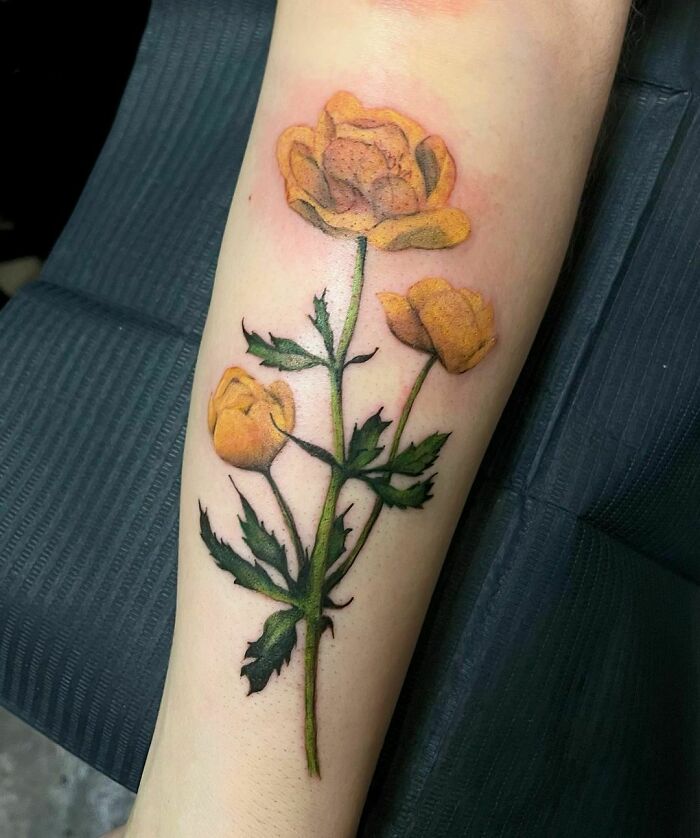 Yellow flower tattoo on forearm, showcasing vibrant petals and green leaves.