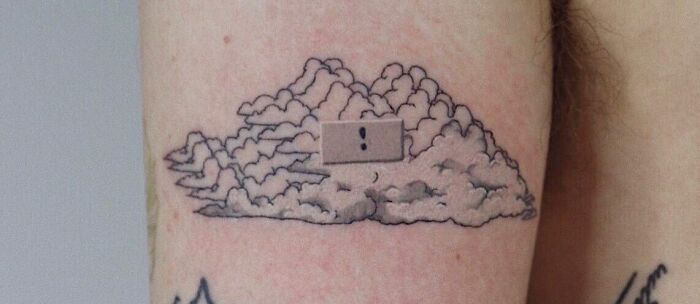 Self-love tattoo featuring clouds and a band-aid with an exclamation mark on an arm.