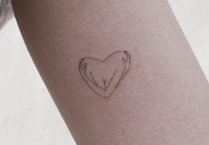 Self-love tattoo of arms hugging to form a heart on the forearm.