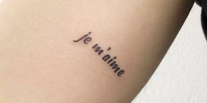 Minimalist self-love tattoo with "je m'aime" script on forearm.