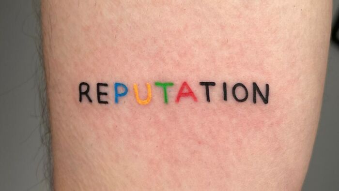 Self-love tattoo with the word "Reputation" in colorful, bold letters on skin, symbolizing personal empowerment.