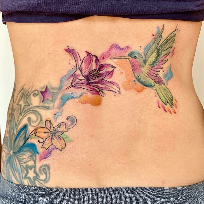 Flower tattoo with a hummingbird on skin, featuring colorful blossoms and intricate designs.