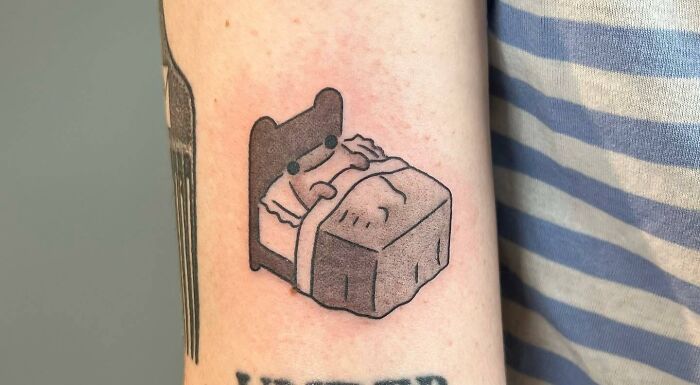 Minimalist self-love tattoo depicting a cozy bed with a cute character on an arm, symbolizing rest and comfort.