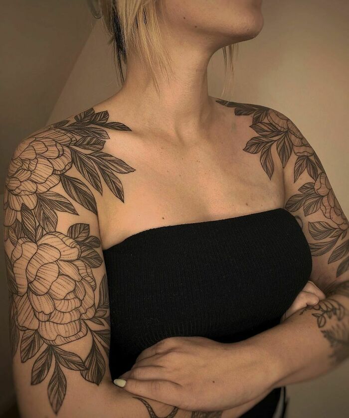 Woman with elegant flower tattoos on shoulders and arms, wearing a black strapless top.