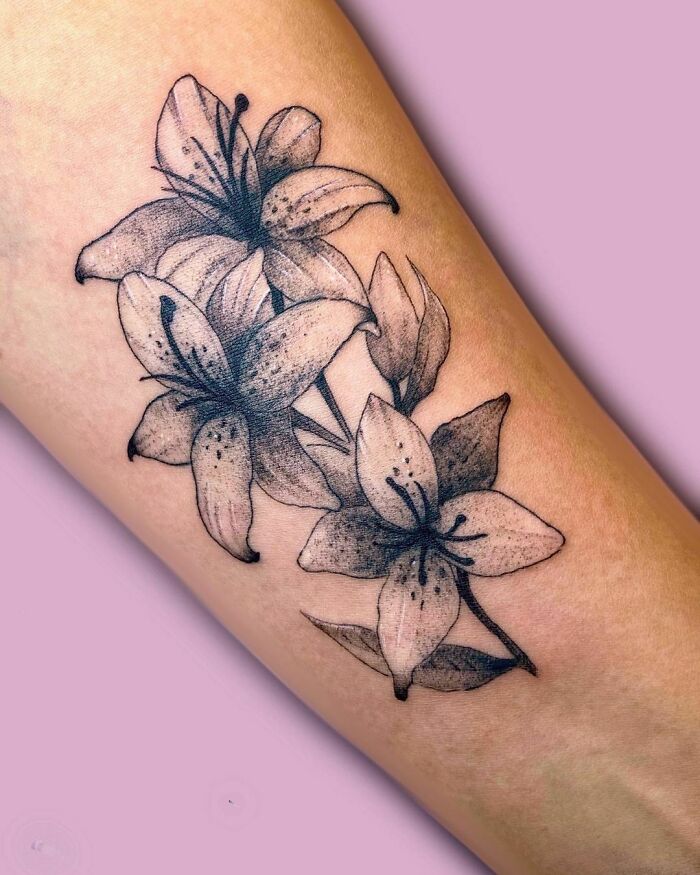 Floral tattoo on forearm featuring detailed lilies, showcasing elegant flower tattoos that seem to blossom on the skin.