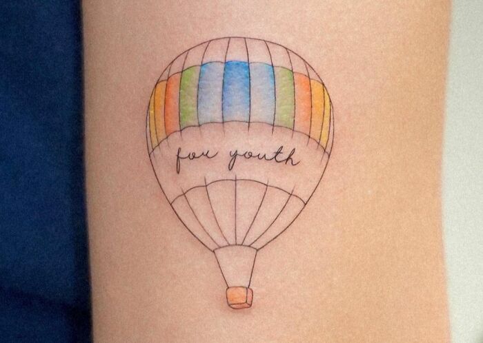 Self-love tattoo of a colorful hot air balloon with the words "for youth" on skin.