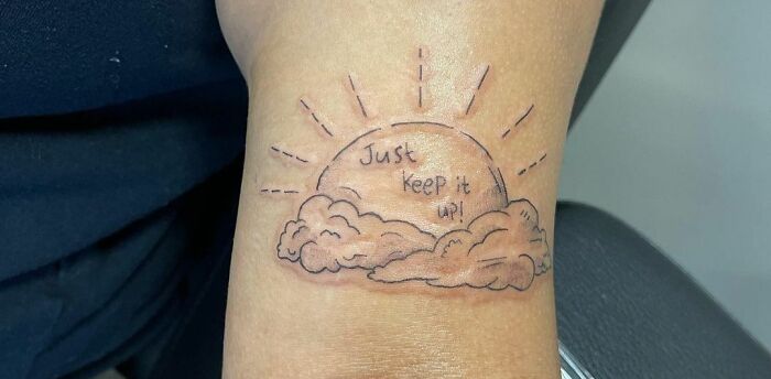 Tattoo of a rising sun with clouds and the words "Just keep it up!" symbolizing self-love and motivation.