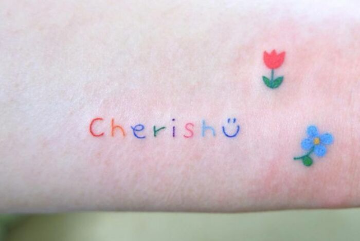 Colorful self-love tattoo with the word "Cherish" and small flower designs on skin.