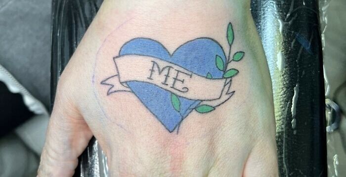 Blue heart tattoo with "ME" banner on a hand, symbolizing self-love and empowerment.